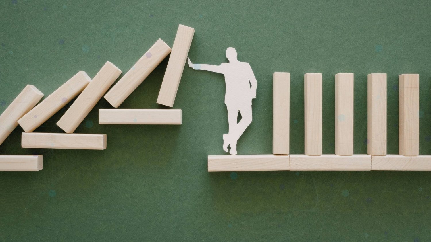 Paper figure holding back falling wooden blocks beside a stable row of upright blocks.